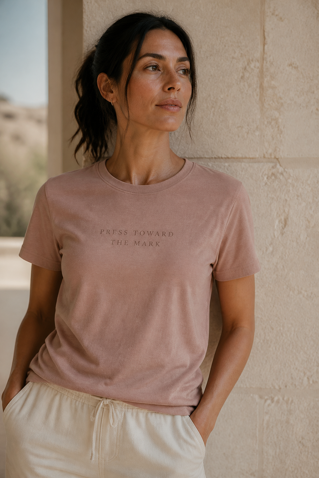 PRESS TOWARD THE MARK, small and letterspaced, tonal on a women’s dusty rose cotton tee.
